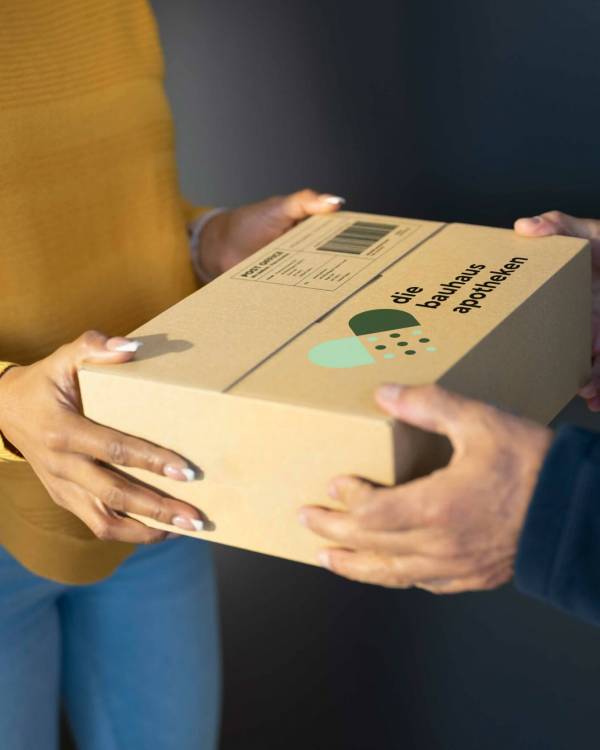 APB_10851_Bilder_Bestelloptionen_sRGB Frau übergibt älterem Mann Paket mit Logo der bauhaus apotheken